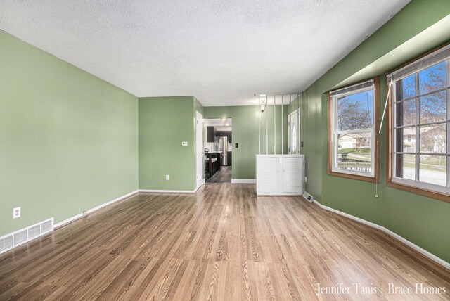 unfurnished living room with baseboards, a textured ceiling, wood finished floors, and visible vents