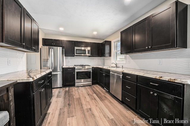 kitchen with light stone counters, a sink, light wood-style flooring, stainless steel appliances, and tasteful backsplash