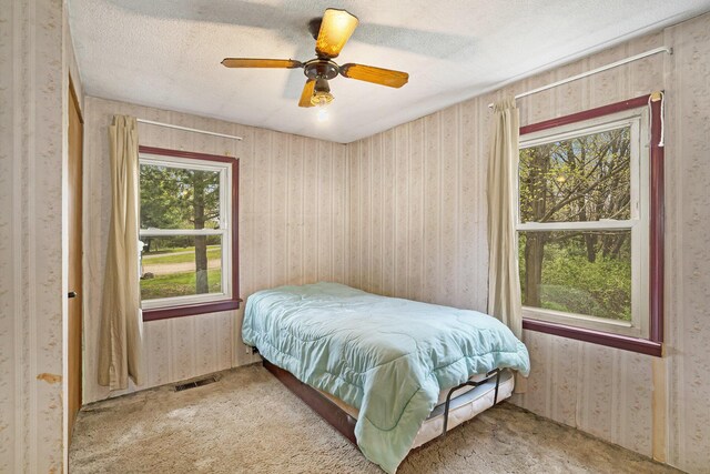 carpeted bedroom with visible vents, a textured ceiling, ceiling fan, and wallpapered walls