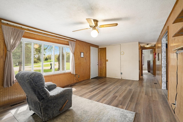 living area with a ceiling fan, a textured ceiling, visible vents, and wood finished floors