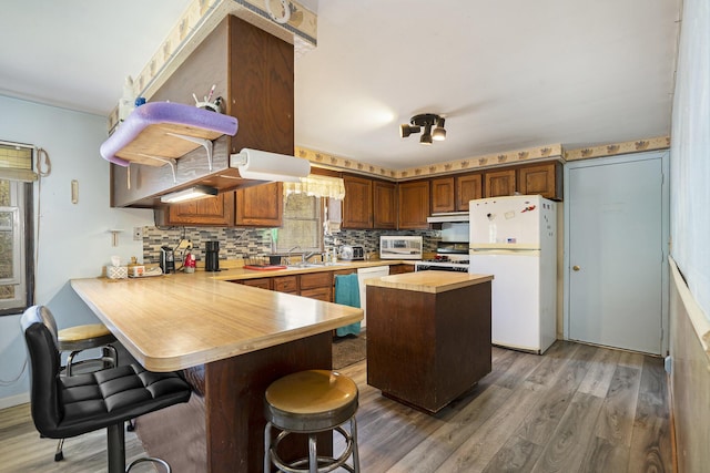 kitchen with a peninsula, wood finished floors, white appliances, a kitchen bar, and tasteful backsplash