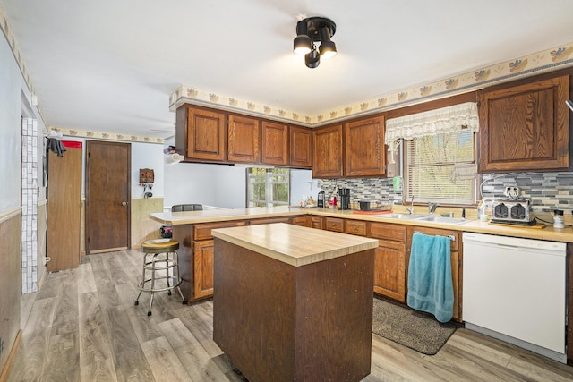 kitchen featuring white dishwasher, a sink, light wood finished floors, and a peninsula