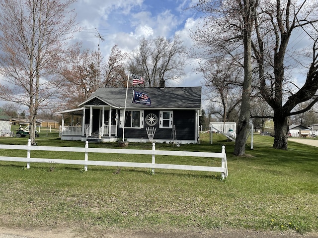 view of front facade with covered porch, a shingled roof, fence private yard, and a front lawn