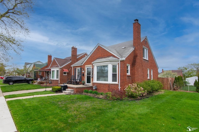 bungalow-style home with brick siding, fence, a chimney, and a front yard