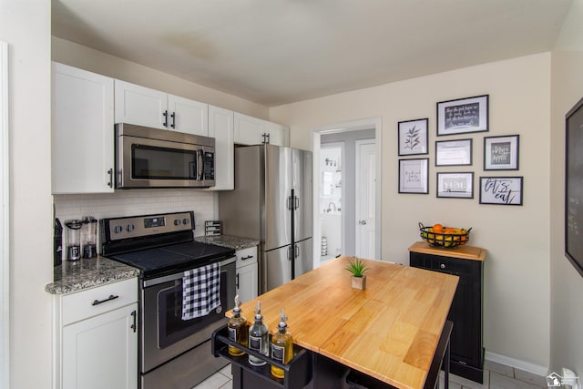kitchen with backsplash, light tile patterned floors, baseboards, stainless steel appliances, and white cabinetry