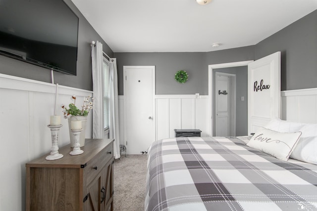 carpeted bedroom featuring a decorative wall and a wainscoted wall