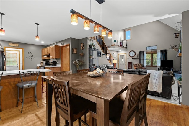 dining room with light wood finished floors, vaulted ceiling, and stairway