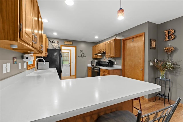 kitchen featuring a breakfast bar, a sink, light countertops, under cabinet range hood, and black appliances