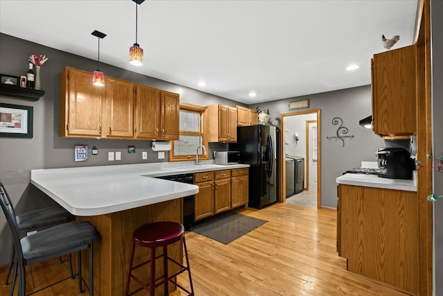 kitchen featuring a breakfast bar area, washing machine and clothes dryer, black appliances, a peninsula, and light wood-style floors