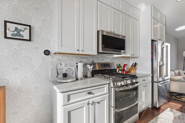 kitchen featuring appliances with stainless steel finishes, light countertops, wallpapered walls, white cabinetry, and dark wood-type flooring