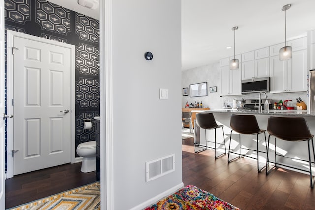 kitchen with visible vents, dark wood-type flooring, stainless steel microwave, and a kitchen breakfast bar