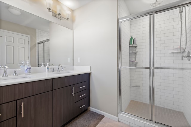 full bathroom with double vanity, baseboards, a shower stall, and a sink