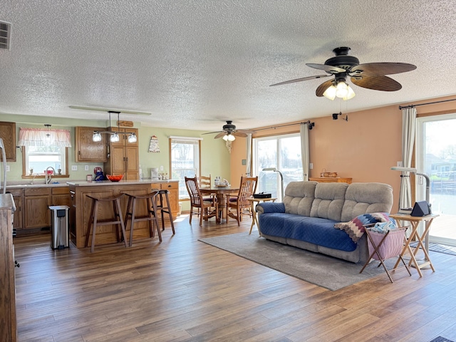 living room featuring a textured ceiling, a ceiling fan, wood finished floors, and visible vents