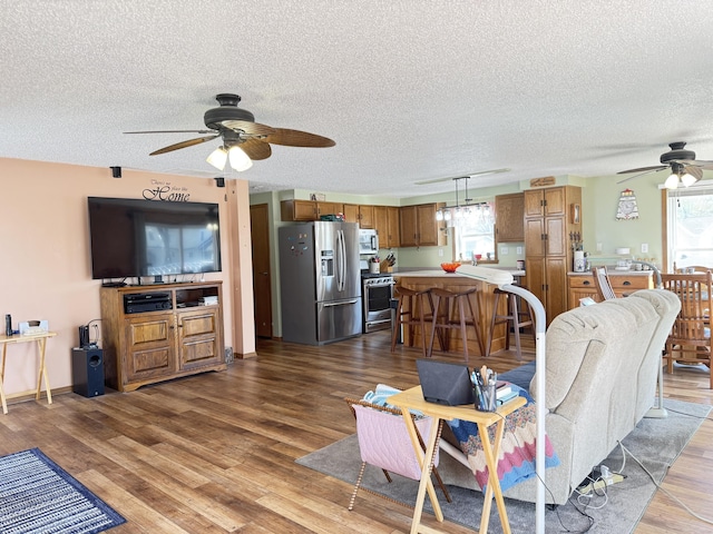 living area with ceiling fan, a textured ceiling, and wood finished floors