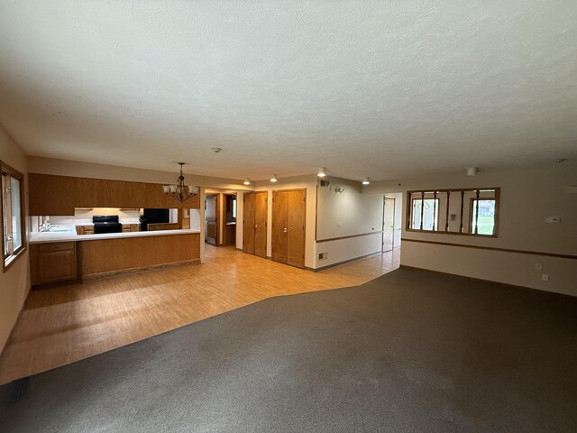 unfurnished living room featuring light colored carpet, light wood-type flooring, a textured ceiling, and a notable chandelier