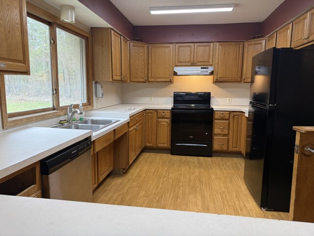 kitchen with a wealth of natural light, under cabinet range hood, a sink, light wood finished floors, and black appliances