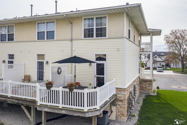 rear view of house with a deck, cooling unit, and stone siding