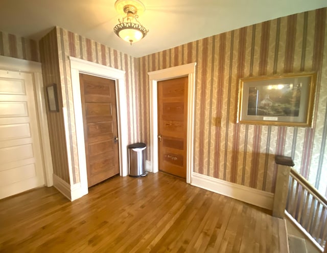 spare room featuring baseboards, wallpapered walls, and wood finished floors