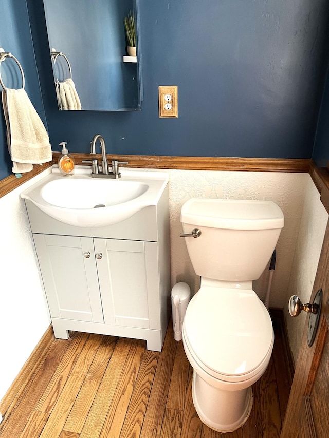 half bathroom with toilet, wood finished floors, and vanity