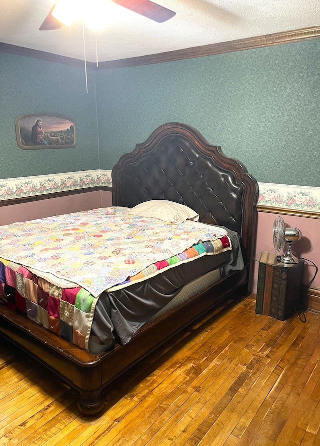 bedroom with ornamental molding, wood-type flooring, a ceiling fan, and wallpapered walls