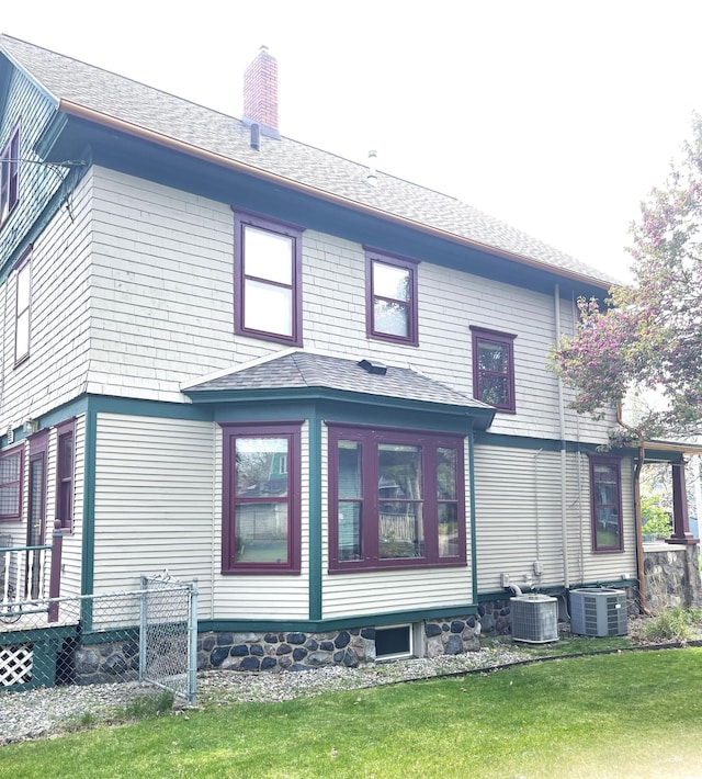 view of property exterior featuring fence, central AC unit, a chimney, and a yard