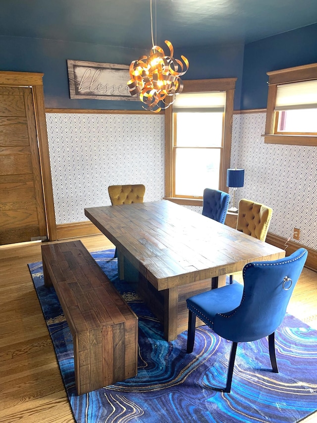 dining space with wood finished floors, a notable chandelier, and wallpapered walls