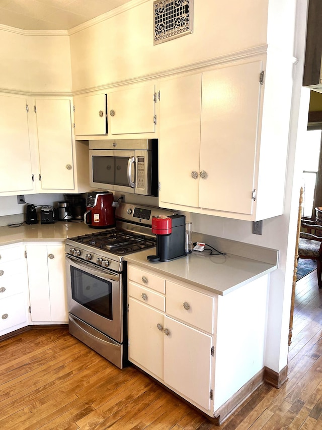 kitchen featuring crown molding, light countertops, white cabinets, light wood finished floors, and stainless steel appliances
