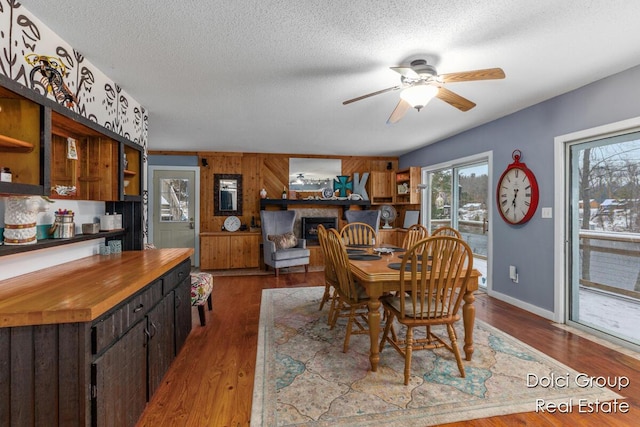 dining area featuring wood walls, dark wood-style flooring, baseboards, a textured ceiling, and a ceiling fan