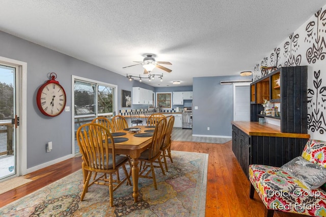dining area featuring a barn door, light wood-style floors, a textured ceiling, a ceiling fan, and baseboards