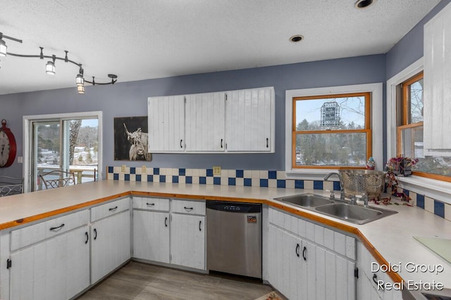 kitchen featuring a textured ceiling, stainless steel dishwasher, a sink, light countertops, and white cabinetry