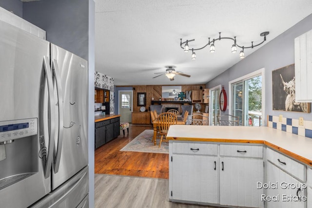 kitchen featuring a peninsula, stainless steel refrigerator with ice dispenser, light countertops, white cabinets, and light wood finished floors