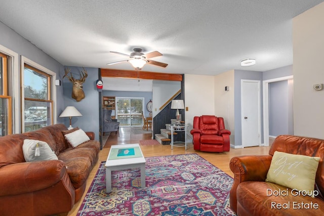 living room with a textured ceiling, ceiling fan, wood finished floors, and stairway