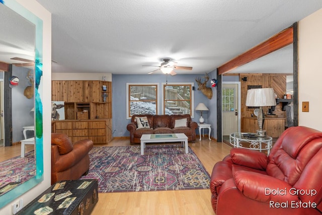 living area with ceiling fan, wood finished floors, and beamed ceiling