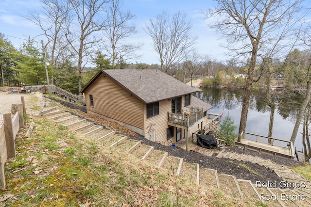 view of home's exterior featuring a shingled roof, a water view, and stairway