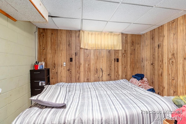 bedroom with concrete block wall, wood walls, and a paneled ceiling