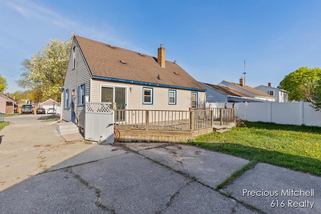 rear view of property with a chimney, roof with shingles, a deck, fence, and a yard