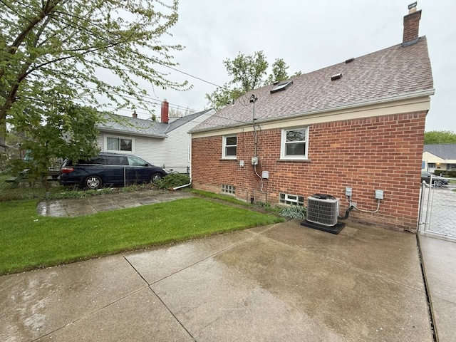rear view of house with brick siding, fence, a lawn, and central AC