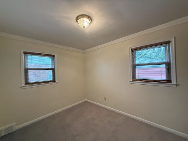 carpeted spare room featuring ornamental molding, baseboards, and visible vents