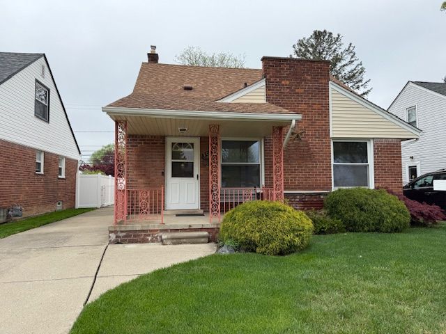 bungalow-style house with covered porch, brick siding, a front yard, a chimney, and a shingled roof