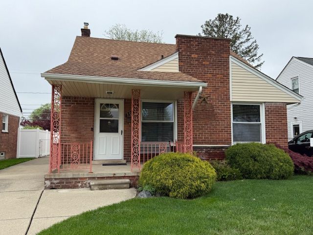 view of front facade with covered porch, brick siding, a chimney, and a front yard