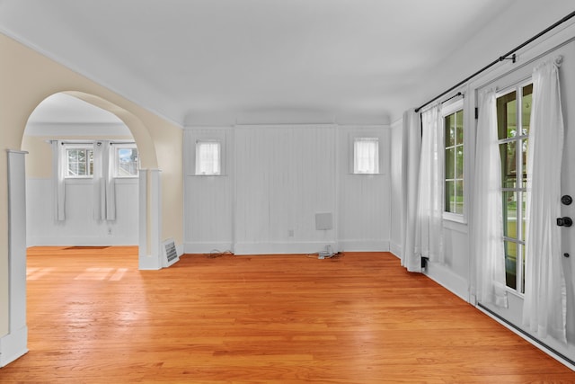 spare room with arched walkways, baseboards, visible vents, and light wood-type flooring