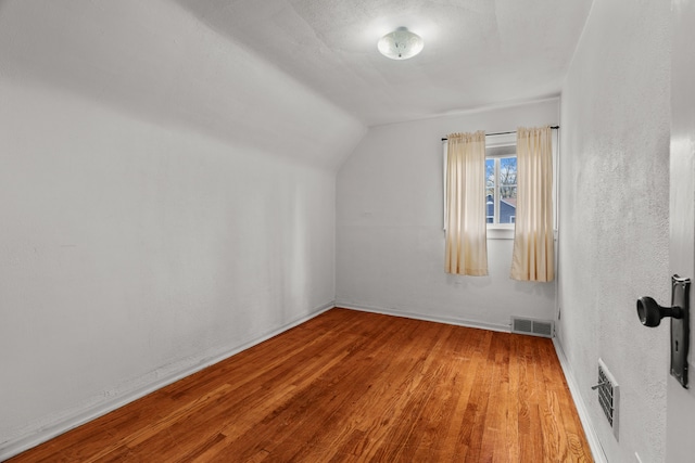 additional living space with baseboards, visible vents, wood finished floors, and lofted ceiling