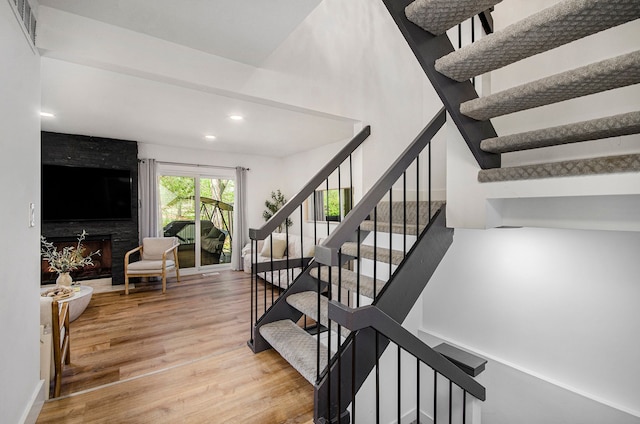 stairway with a towering ceiling, recessed lighting, wood finished floors, and visible vents
