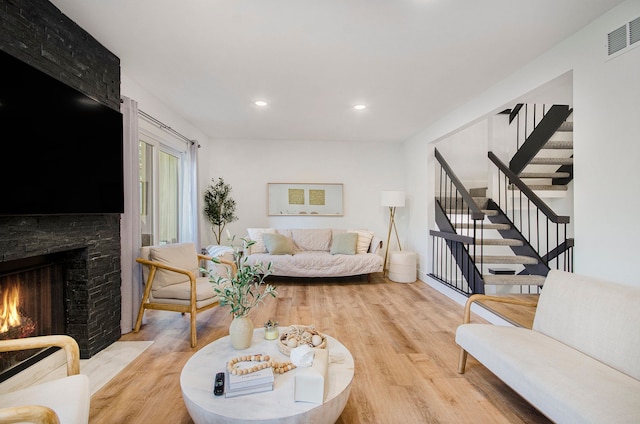 living room featuring a stone fireplace, visible vents, stairs, light wood-style floors, and recessed lighting