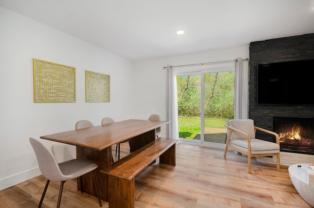 dining space featuring baseboards, visible vents, a large fireplace, and light wood-type flooring