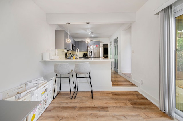 kitchen featuring a kitchen breakfast bar, light wood-type flooring, gray cabinetry, a peninsula, and stainless steel appliances