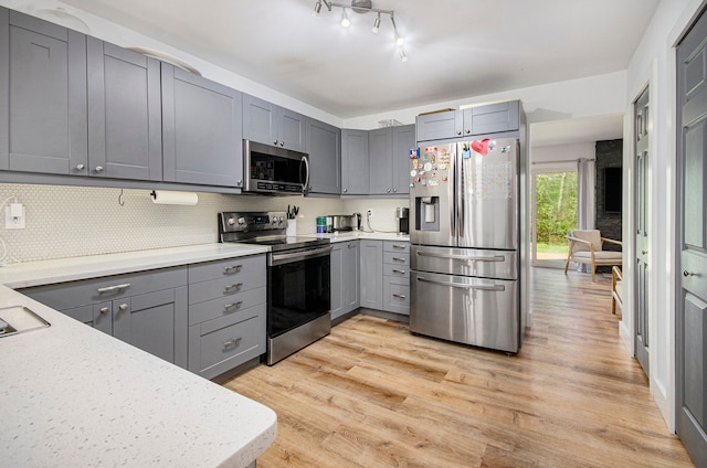 kitchen with light wood-style floors, decorative backsplash, gray cabinets, and appliances with stainless steel finishes