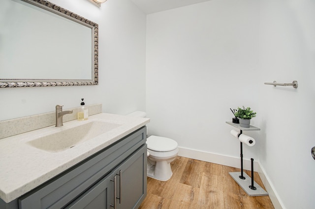 half bath with vanity, baseboards, toilet, and wood finished floors