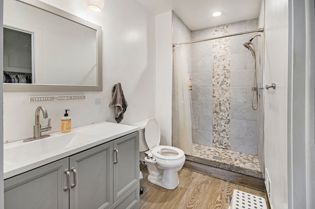 full bath featuring vanity, toilet, wood finished floors, visible vents, and tiled shower