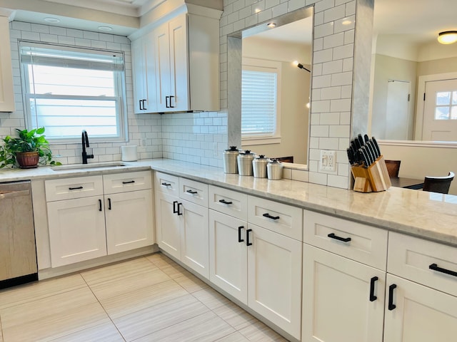 kitchen featuring tasteful backsplash, stainless steel dishwasher, a sink, light tile patterned floors, and white cabinetry
